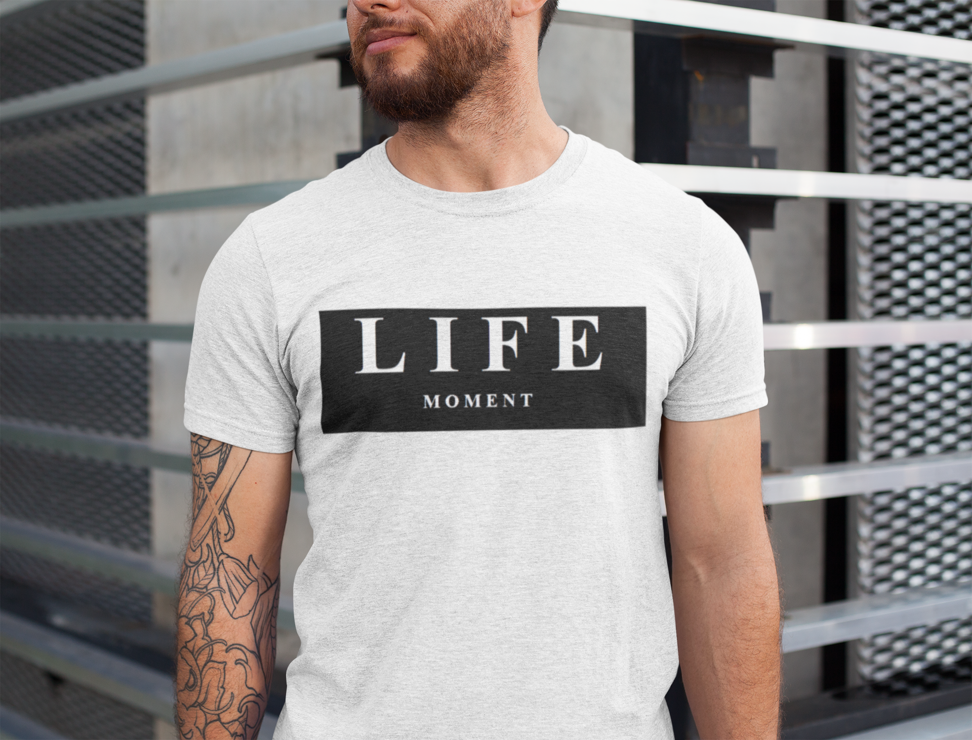 A man with tattoos on one arm wears a heathered Life Moment T-shirt in a mockup.